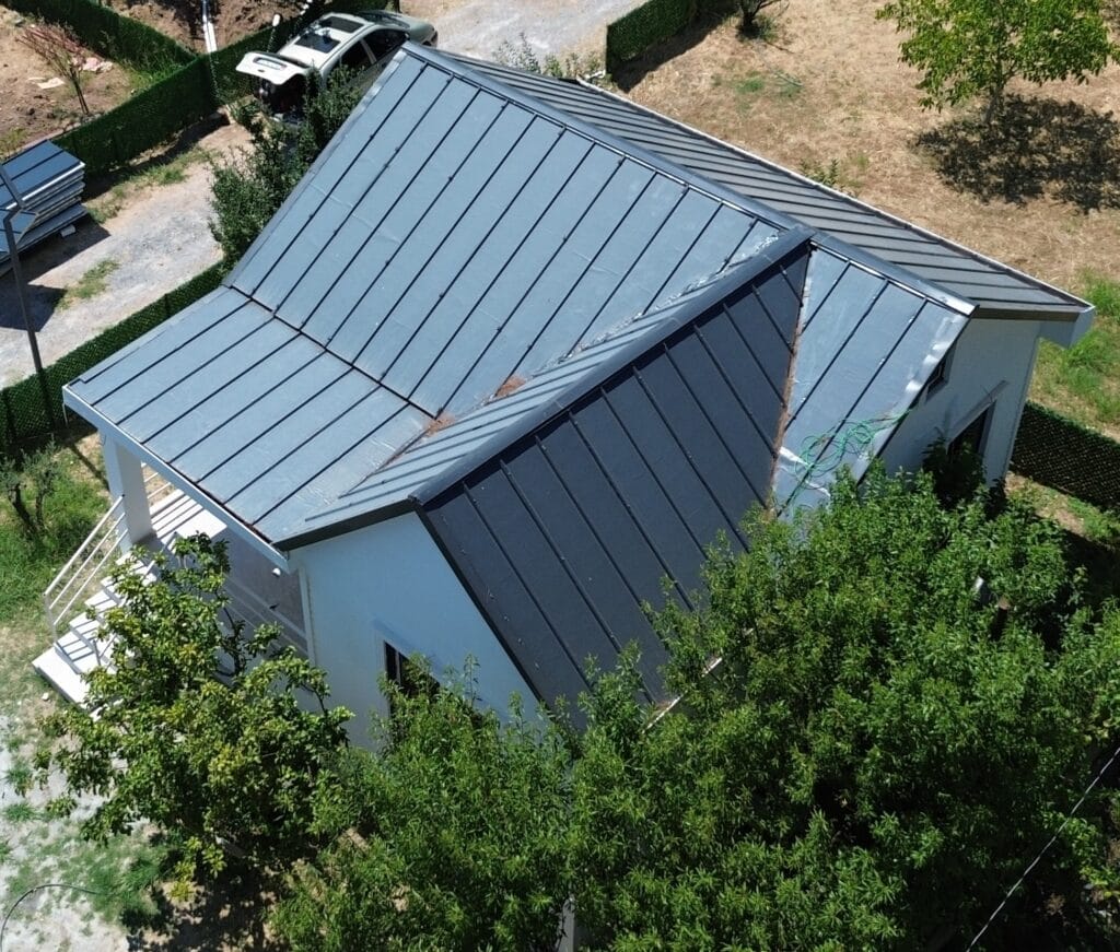 Aerial view of a steep residential metal roof with minimal clearance from surrounding trees, creating a complex scenario for zero-error solar panel placement.